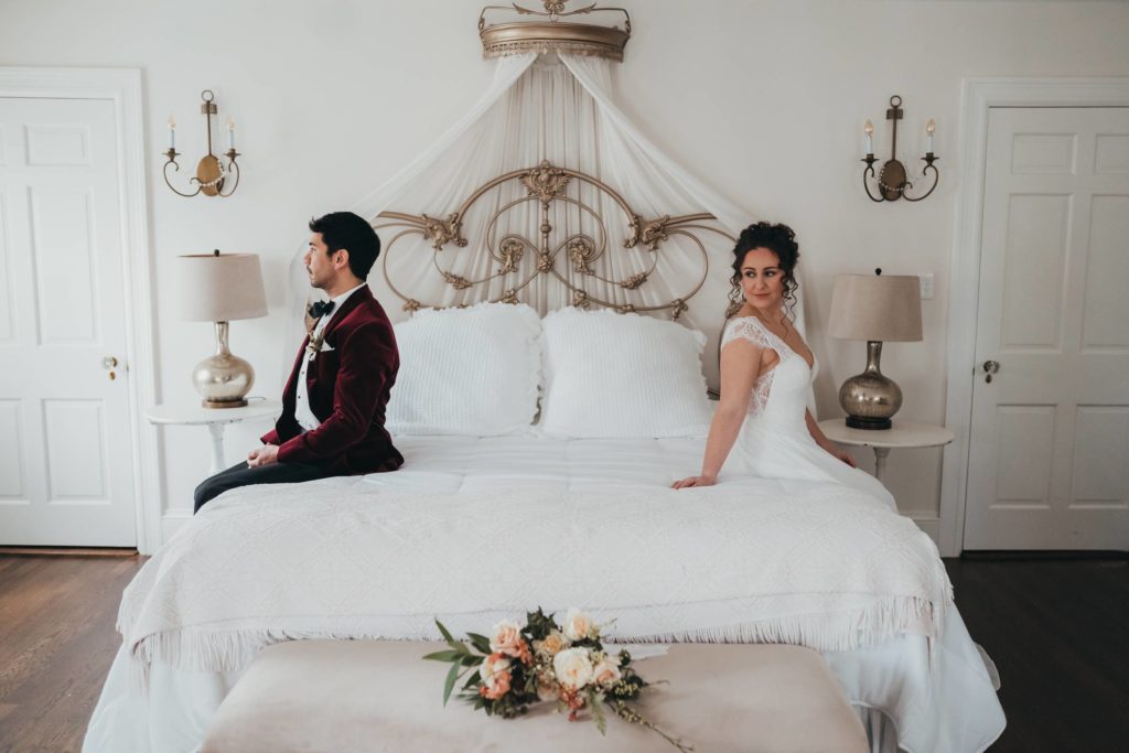 Bride and groom sit on bed facing away from each other