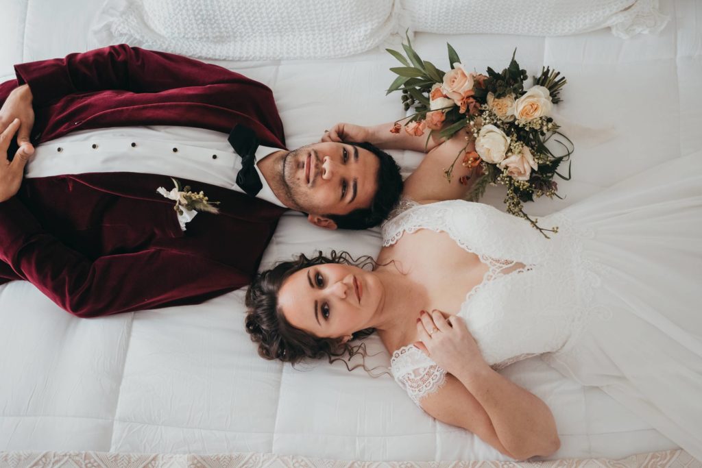 Bride and Groom lay on bed with heads next to one another looking up at camera