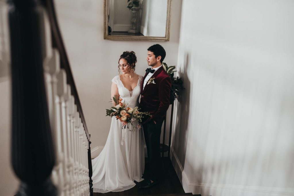 Groom looks at bride as she looks away while standing on a staircase landing