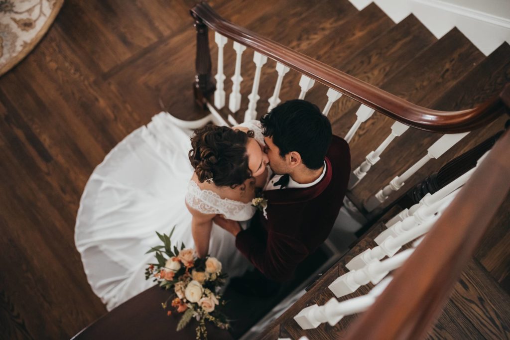 Bride and groom stand in corner of stairwell and share a kiss
