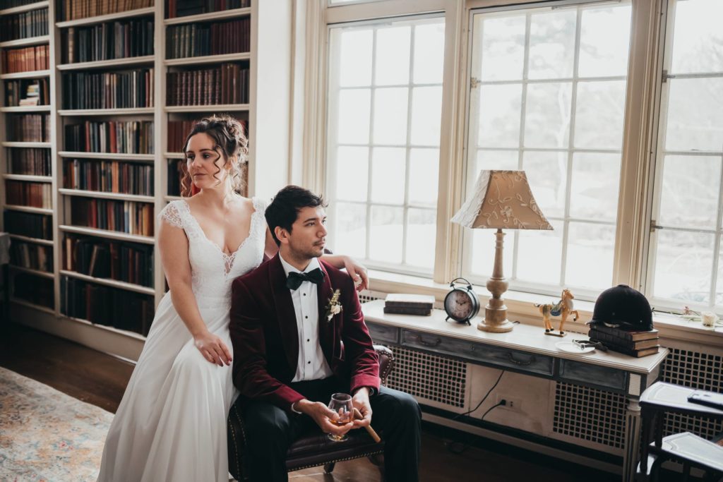 Bride and Groom sit together on a leather chair in the library