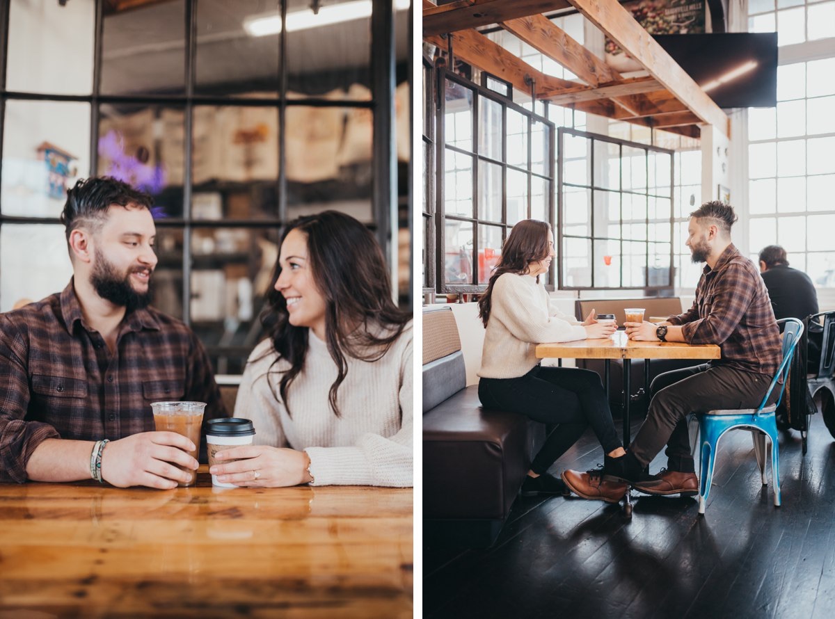 A couple sits together on the same side of the table at a coffee shop smiling and laughing.
