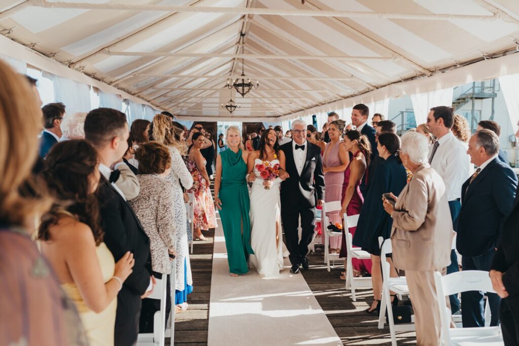 Bride laughing as she walks down the aisle with both of her parents in Newport Rhode Island